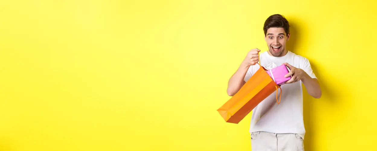 concept-holidays-celebration-young-man-looking-surprised-as-take-out-gift-from-shopping-bag-s